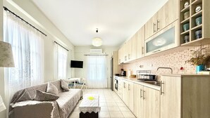 Ett kompakt bostadsutrymme med en soffa, ett litet bord, en köksdel med skåp och en tv.
