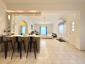 A modern living space with a kitchen area, dining table, and a bedroom with a bed and a sofa. - Villa Fenia (Amorgos)