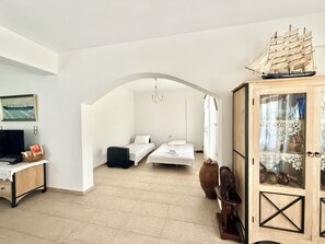 A room with two beds, a television, a cabinet with decorative items, and a ship model. - Villa Fenia (Amorgos)