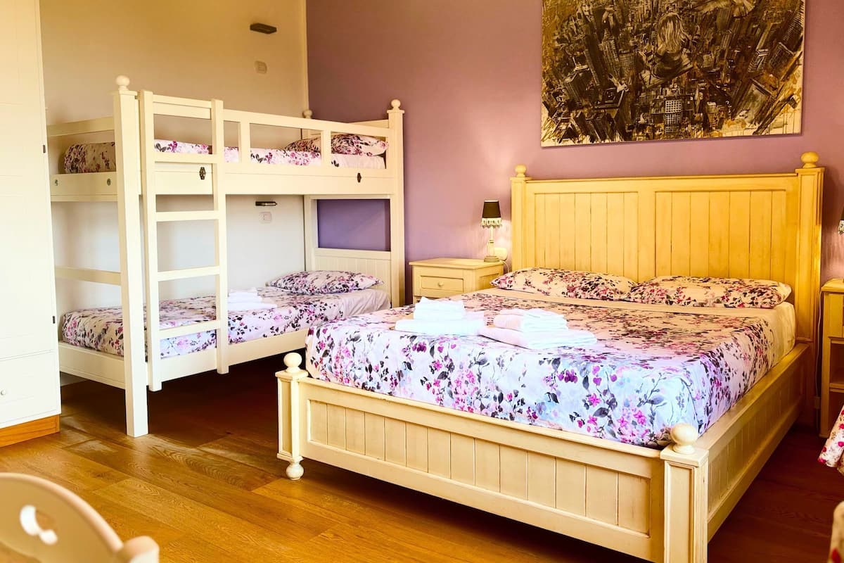 A room with bunk beds, a single bed, a nightstand, a lamp, and a painting on the wall.