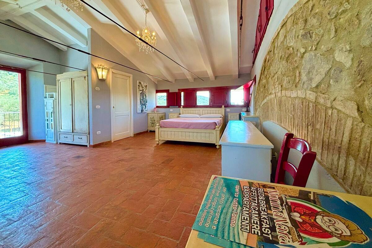A bedroom with a bed, a dresser, a nightstand, a chair, a table, and a chandelier.