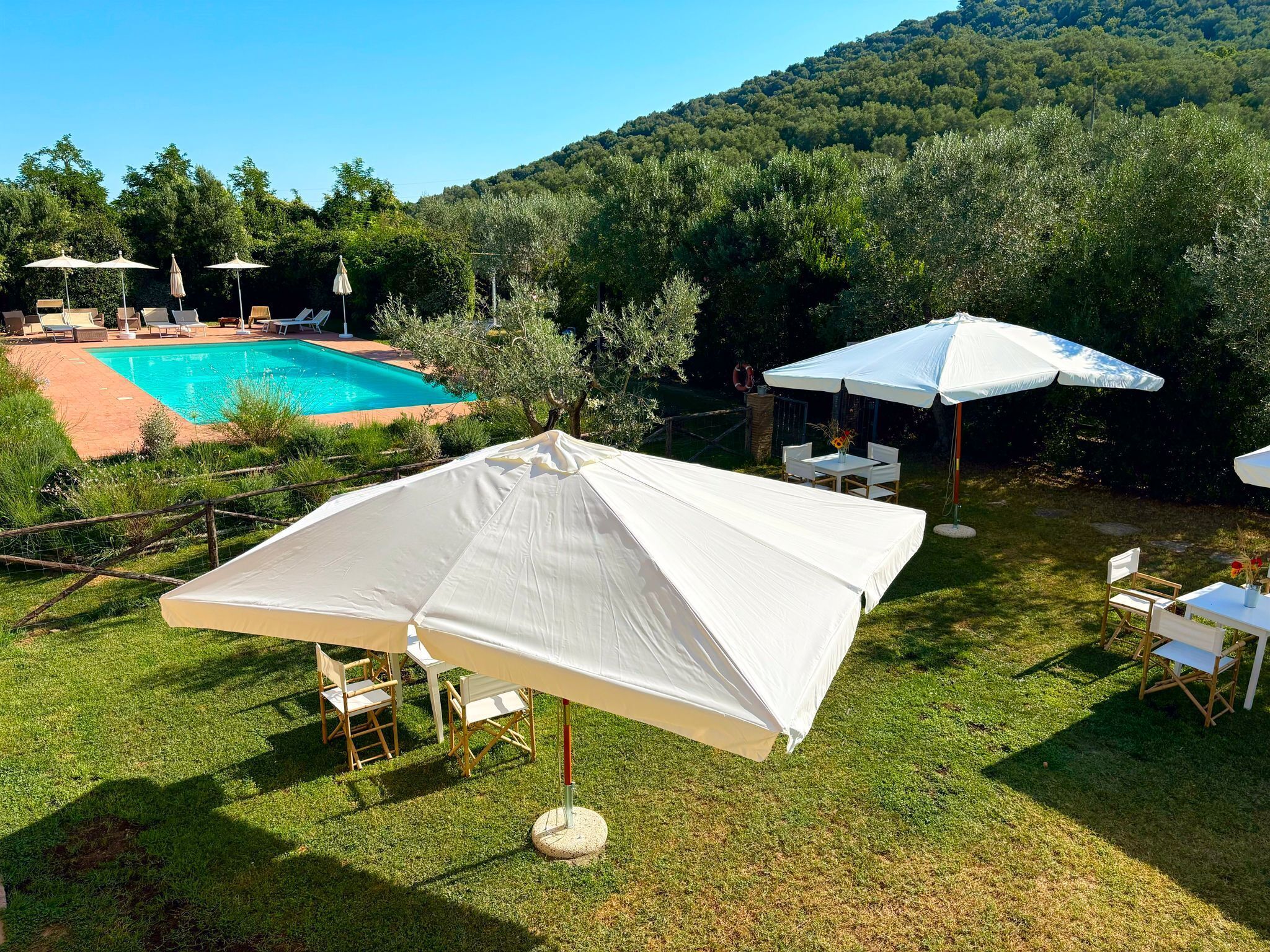 Zona de piscina con sombrillas, sillones reclinables y una mesa con sillas.