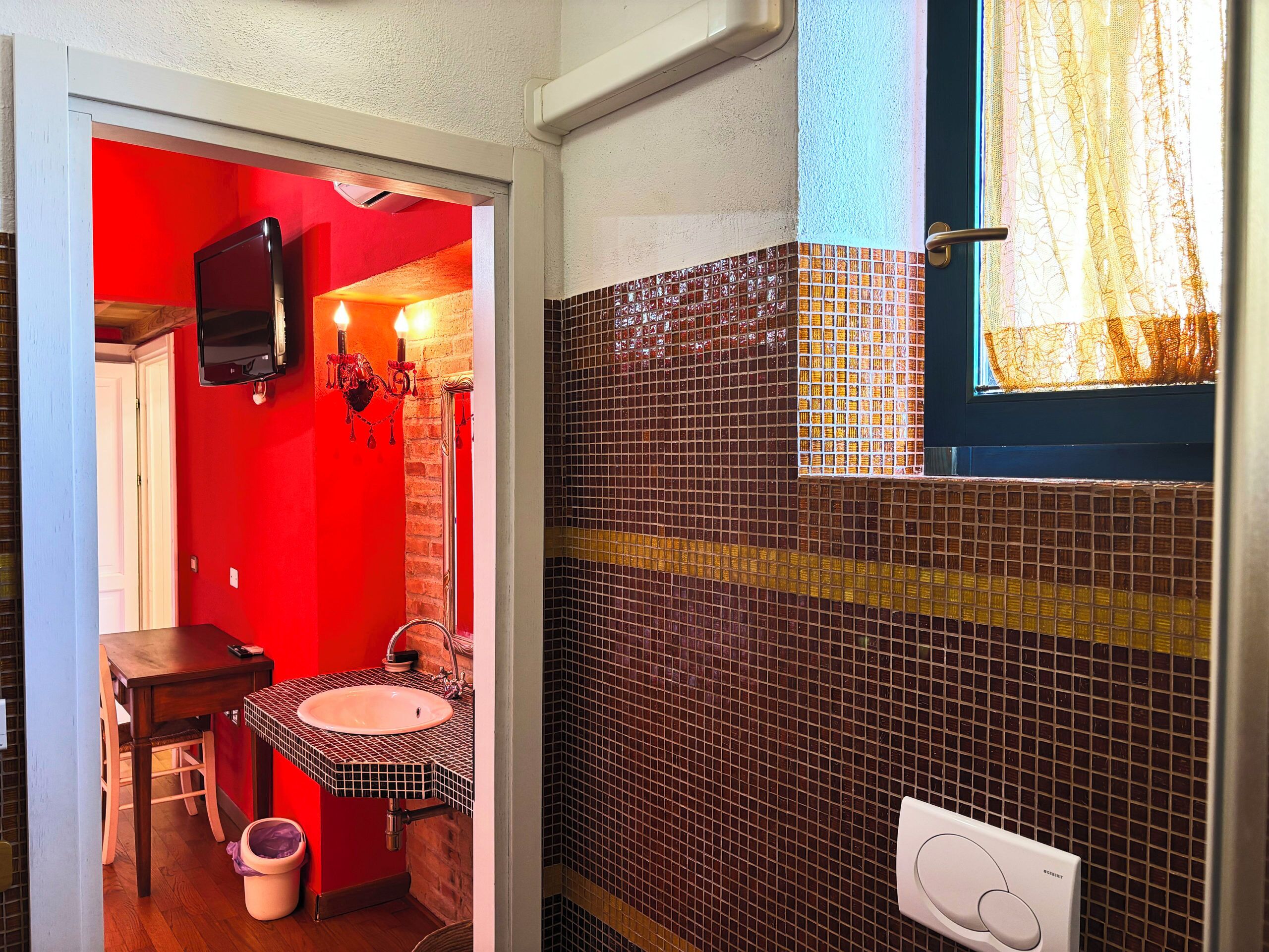 A bathroom with a red wall, a tiled sink area, and a window with curtains.