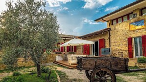 A rustic stone building with a courtyard, a wooden cart, and a tree. - NonnaNara (Grosseto)