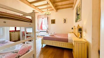 Una habitación con literas, un escritorio, una silla, una mesita de noche con lámpara y una ventana con cortinas.