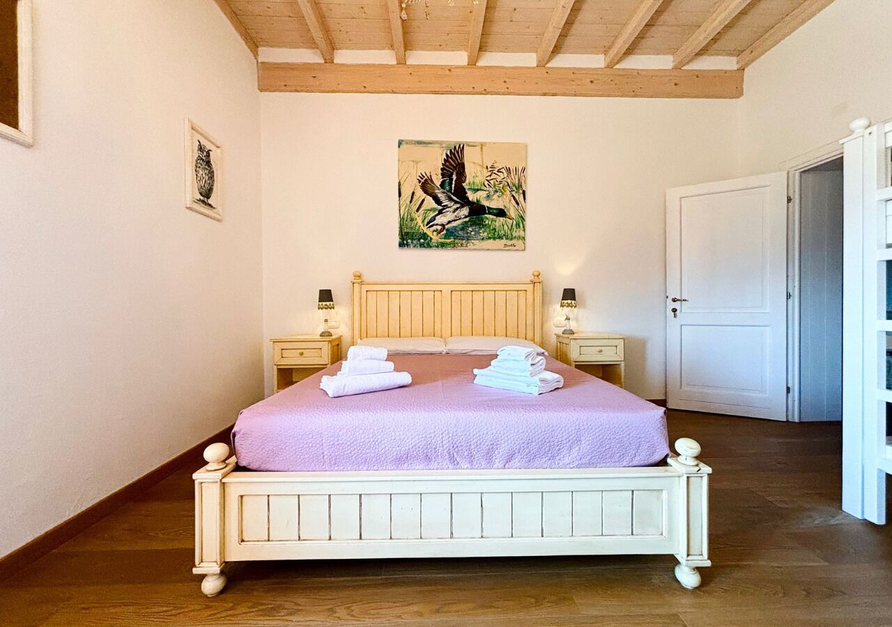 Une chambre avec un lit en bois, des murs blancs, un tableau au-dessus du lit et une porte sur le côté droit.