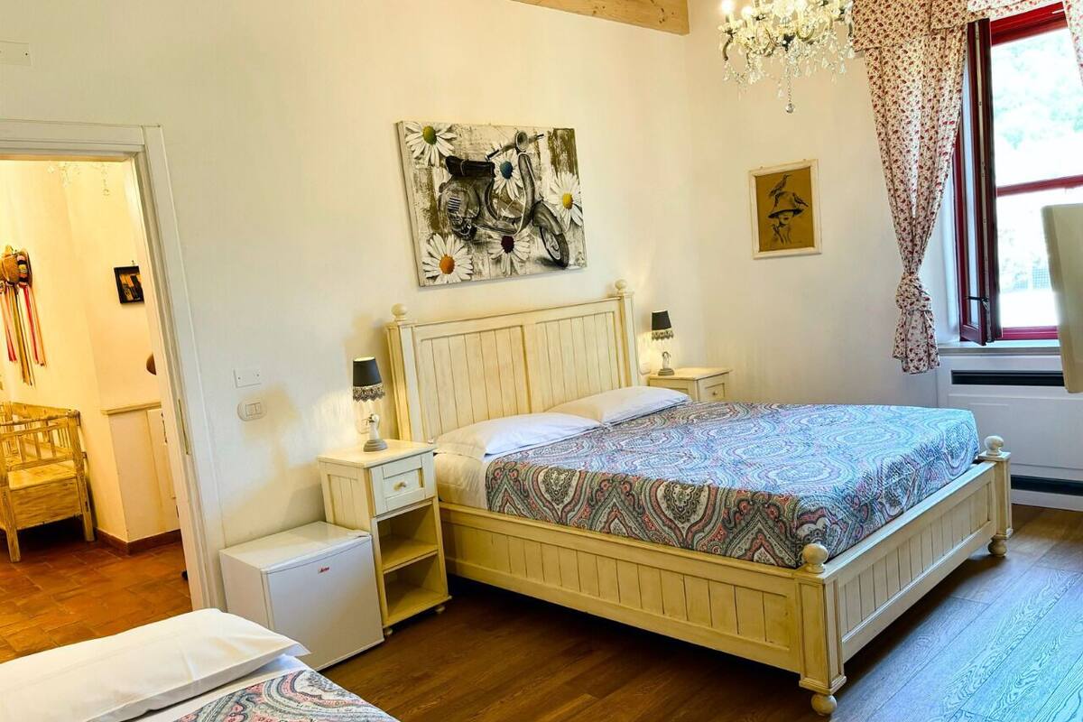 A bedroom with a wooden bed, bedside tables, a nightstand, a chair, a small white cabinet, and a window with curtains.