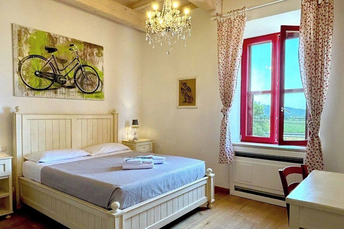 A bedroom with a bed, a bicycle painting, a chandelier, a window with curtains, and a radiator.