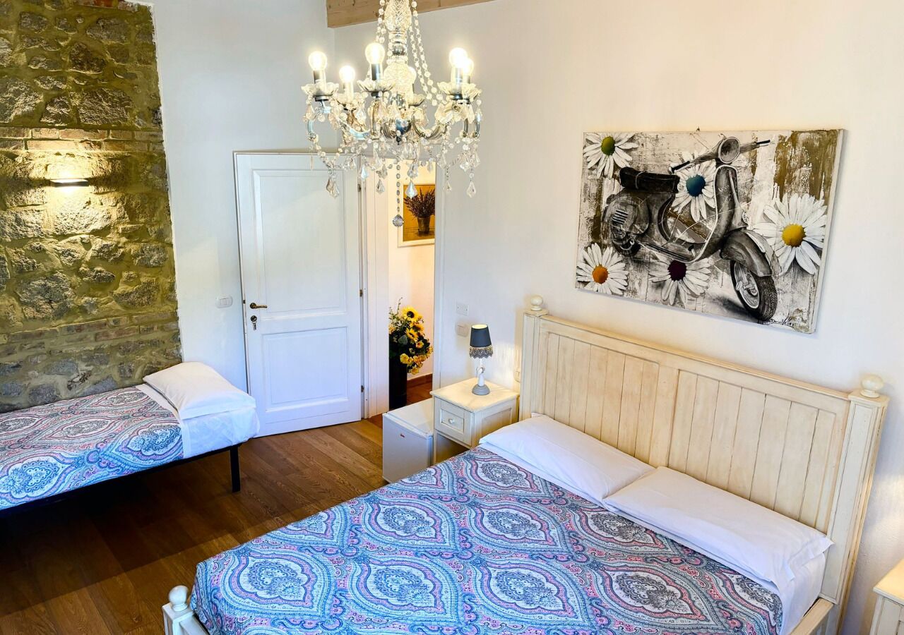 A bedroom with two beds, a chandelier, a wall-mounted artwork, and a stone wall.