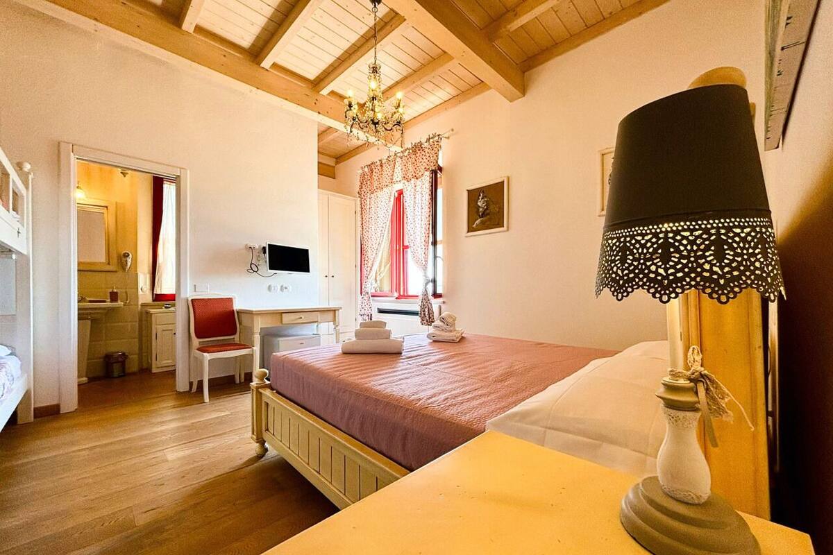 A bedroom with a bed, a desk, a chair, a lamp, and a window with curtains.