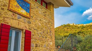 A stone building with a red shuttered window, a colorful mosaic, and a staircase leading to a hilltop view. - NonnaNara (Grosseto)