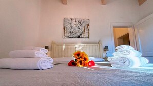 A hotel room with a bed, towels, a painting, and a vase with flowers. - NonnaNara (Grosseto)