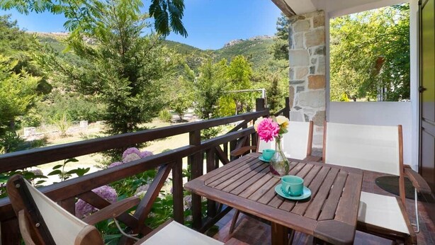Una terraza de madera con una mesa y sillas, con vista a un paisaje montañoso.