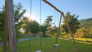Un columpio de madera en un parque con césped, árboles y cielo despejado.