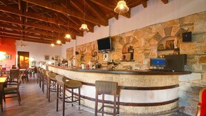 Un área de bar con paredes de piedra, vigas de madera en el techo y taburetes.
