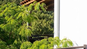 A balcony with a view of a mountainous landscape, a white building with a red roof, and green foliage.