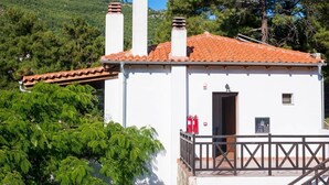 A white building with a red-tiled roof, two chimneys, a balcony with a railing, and a door.