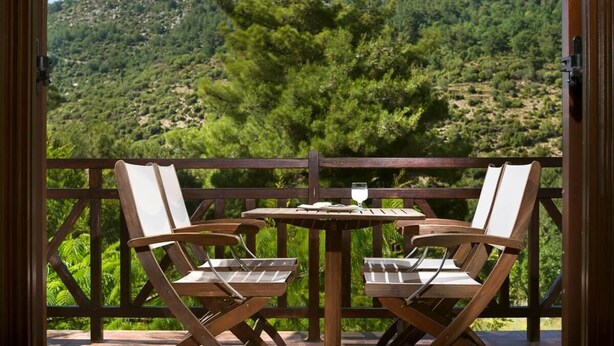 A wooden deck with two chairs and a table, overlooking a mountainous landscape.