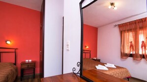 A room with a wooden bed, a small bedside table, a mirror, and a window with sheer curtains.