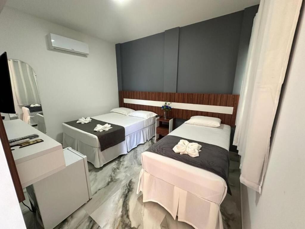 A hotel room with two beds, a desk, a mirror, and an air conditioning unit.