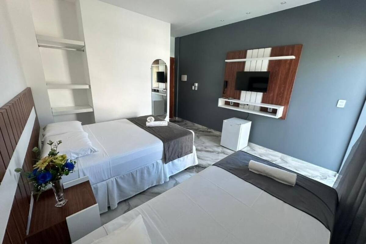 A modern hotel room with two beds, a TV, a mirror, and a small desk.