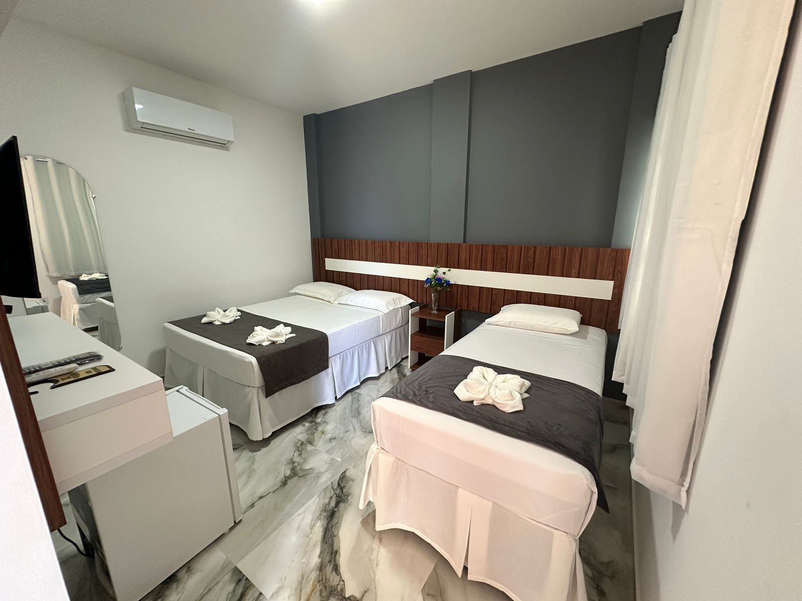 Et hotelværelse med to senge, et skrivebord, en stol, et spejl og en aircondition.