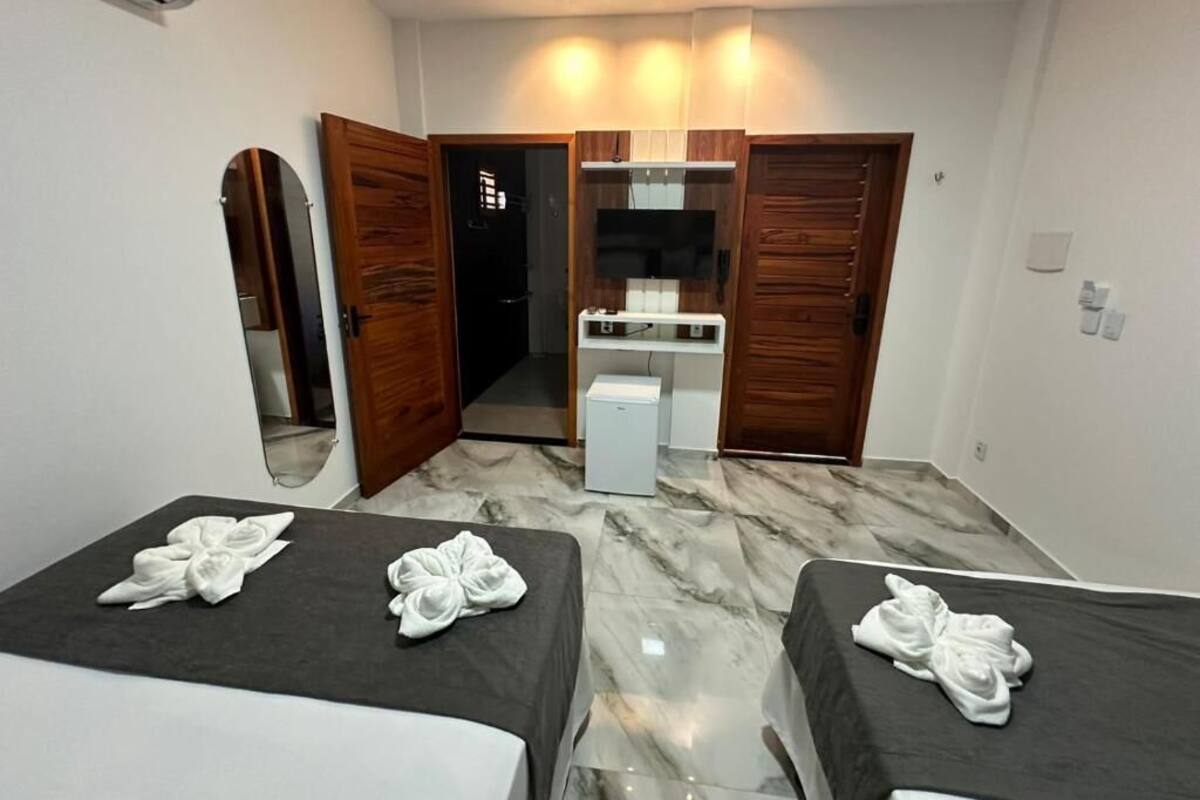 A hotel room with two beds, a small kitchenette, a mirror, and a door leading to a bathroom.