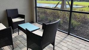 Parvekkeella on rottinkihuonekaluja, pöytä ja suuri ikkuna, josta avautuu näkymä golfkentälle ja vesistöön.