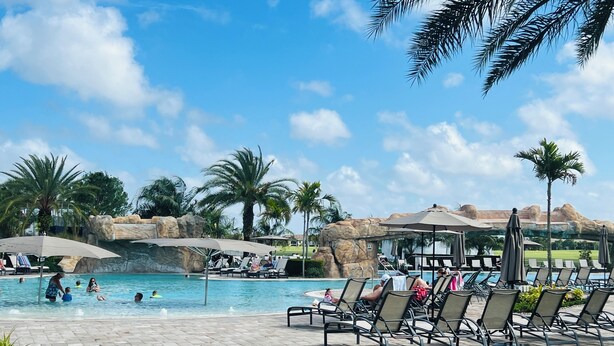 Allasalue, jossa on aurinkotuoleja ja -varjoja, ja jota ympäröivät palmut ja kalliojyrkänteet.