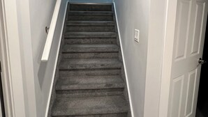 A staircase with carpeted steps leading to a landing, white walls, and a door on the right. - Hidden Gem 💎 Stylish Suite w/ All-Inclusive Comfort” (Regina)