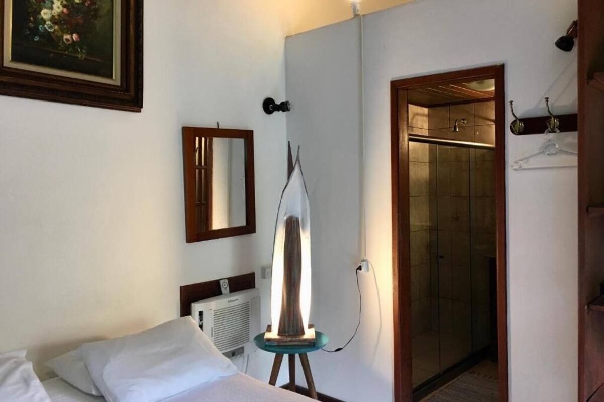 Quarto de hotel com cama, quadro, espelho, luminária e porta para um banheiro.