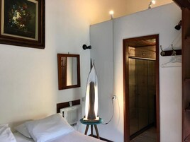 A hotel room with a bed, a painting, a mirror, a lamp, and a door leading to a bathroom.