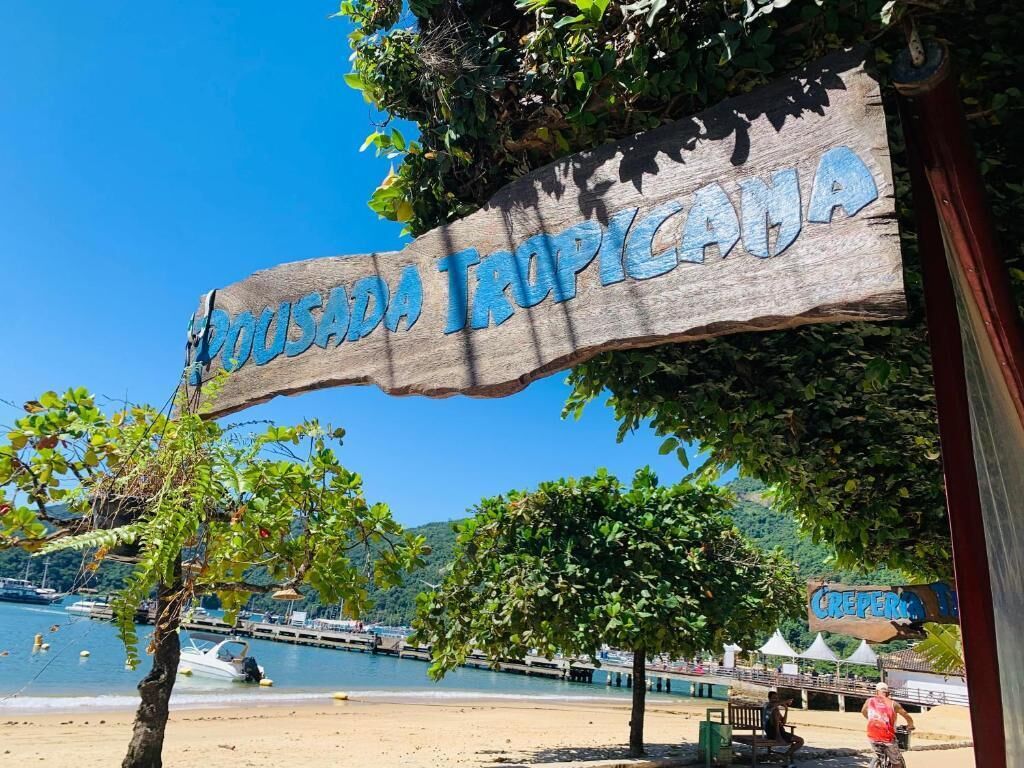 A wooden sign with 'TROPICALA' written on it, a beach, boats, and a clear blue sky.