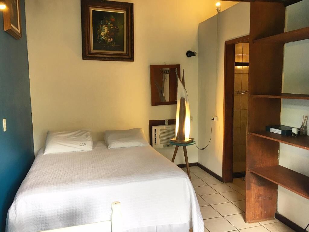 A hotel room with a bed, a bedside lamp, a mirror, and a wooden shelf.