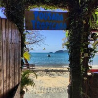 A wooden gate with a sign reading 'Pousada Tropicala' leading to a beach.