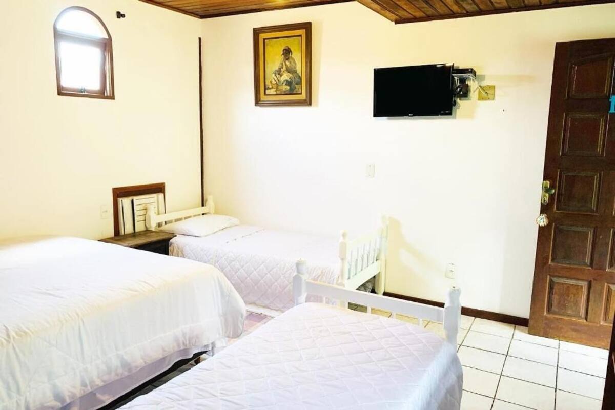 Quarto com duas camas, televisão fixada na parede, porta de madeira e uma janela pequena.