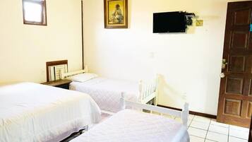 A room with two beds, a television mounted on the wall, a wooden door, and a small window.