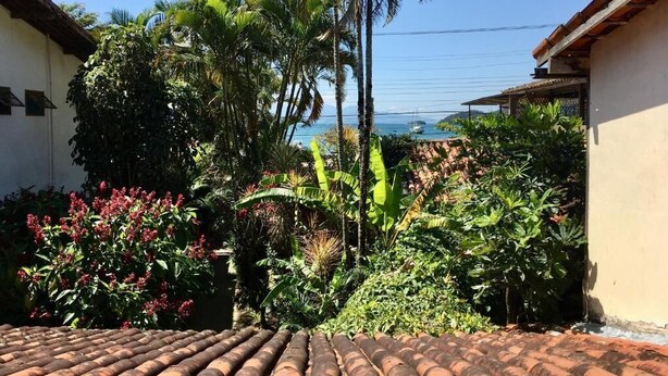 Un cortile con tetto in tegole, circondato da vegetazione lussureggiante e vista sull'oceano.