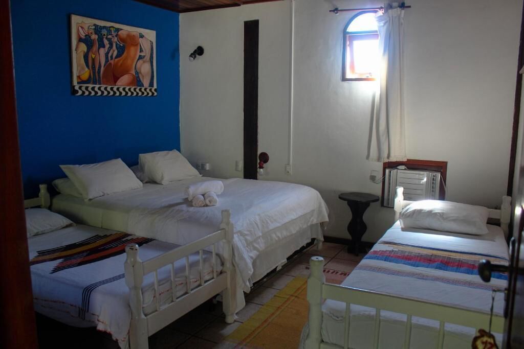 Quarto com duas camas, janela com cortinas, radiador e um quadro na parede.