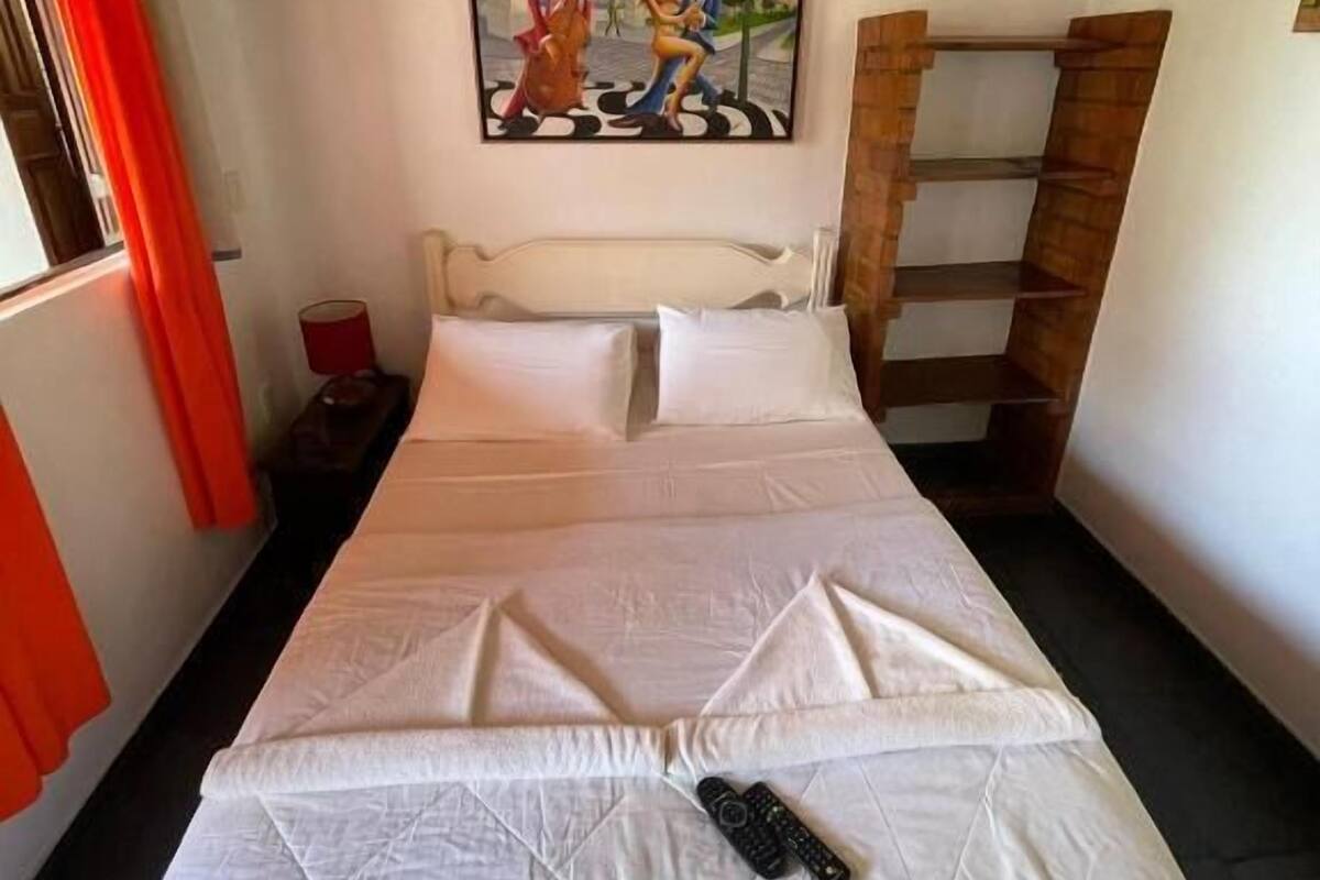 Quarto com cama, pintura, cortina vermelha e escada de madeira.