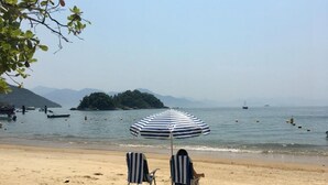 Una spiaggia con due lettini a righe e un ombrellone, cielo sereno e barche in acqua.