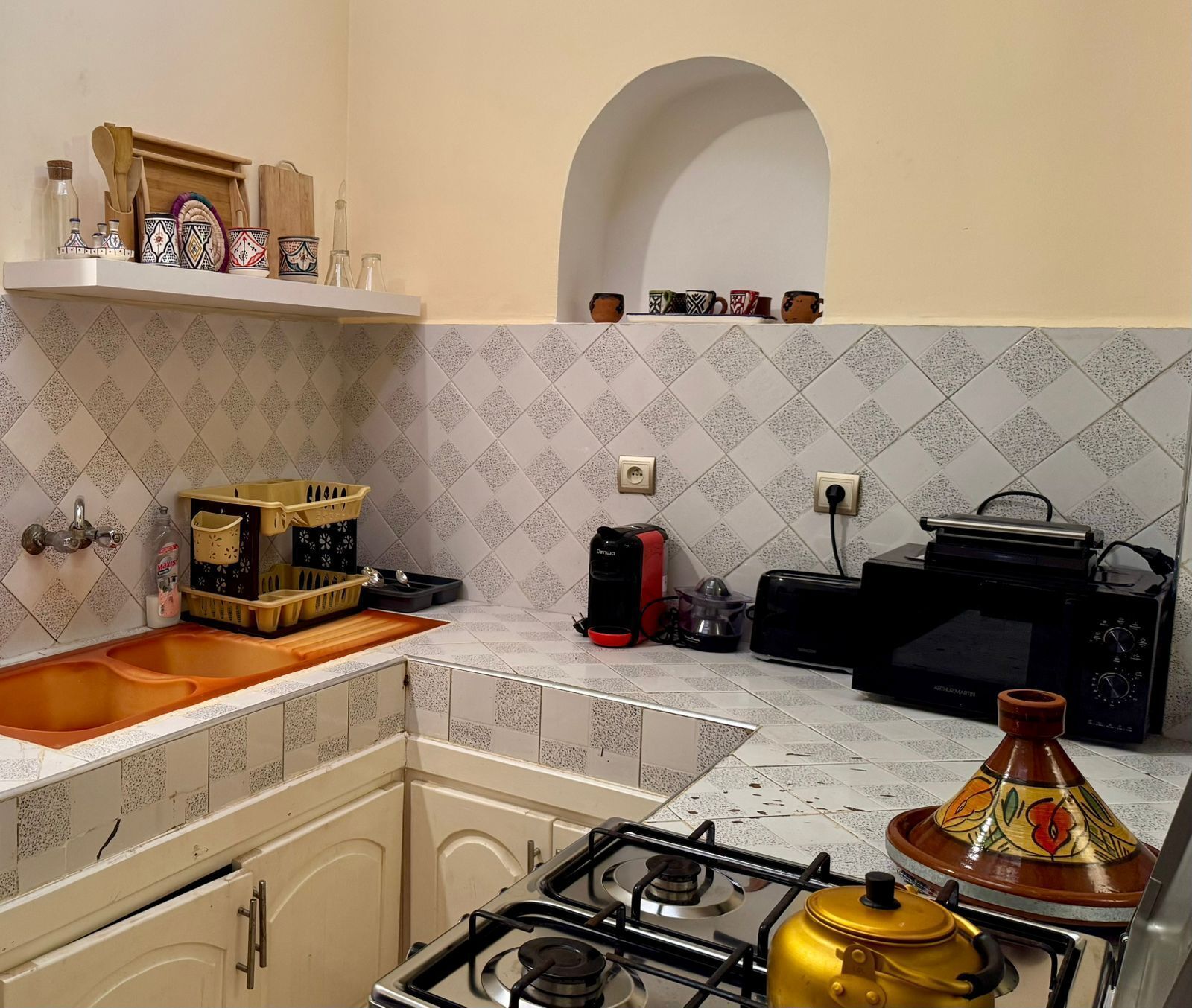 Une cuisine équipée d’une cuisinière à gaz, d’un four à micro-ondes, d’un évier et d’une étagère contenant des ustensiles de cuisine.