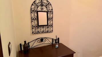 Una habitación con una pequeña mesa de madera, un espejo metálico decorativo y una botella de gel hidroalcohólico.