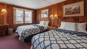 Una habitación con dos camas, paredes de madera, un ventanal, un escritorio y dos lámparas fijadas a la pared.