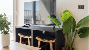 Een moderne woonkamer met een flatscreen televisie, houten meubels en grote groene planten.