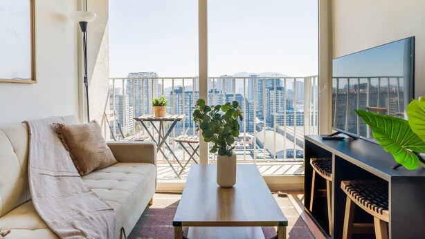 Een balkon met een bank, een bijzettafeltje, een televisie en uitzicht op de stad.