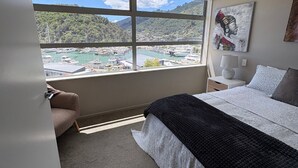 Un dormitorio con un ventanal grande, una cama, una mesita de noche, una lámpara y un cuadro.