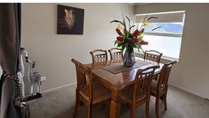 Un comedor con una mesa y sillas de madera, un jarrón con flores, un cuadro de un leopardo en la pared y vistas a través del ventanal.