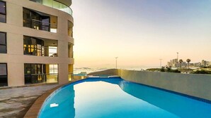 A modern building with a swimming pool, balconies, and a view of the ocean. - Luxury Beachfront Apartment with Panoramic Ocean Views – Strand Ocean View 1004 (Strand)