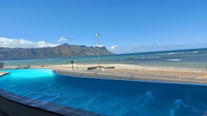 A swimming pool with a view of the beach and mountains. - Luxury Beachfront Apartment with Panoramic Ocean Views – Strand Ocean View 1004 (Strand)